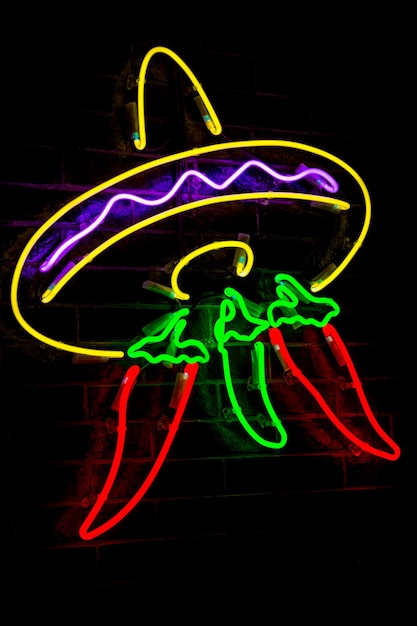 Gloeiende Neon gestileerde Mexicaanse sombrero en rode pepers en vage lichten op zwarte bakstenen muur achtergrond. Donkere tinten vintage afbeelding.