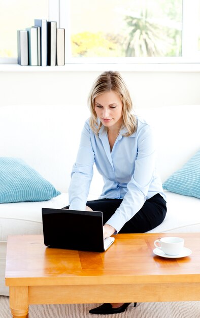 Gloeiende onderneemster die haar laptop zitting op een bank met behulp van