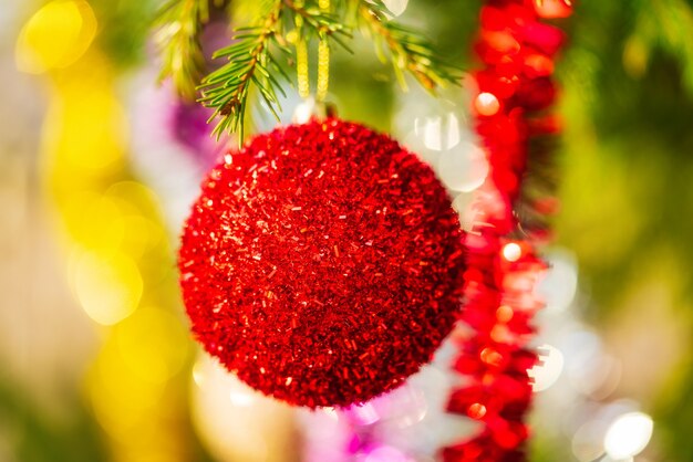 Gloeiende rode kerstbal en kleurrijke glanzende klatergoud hangend aan de tak van de boom. Vergrote weergave Xmas feestelijke compositie voor Happy New Year. Selectieve focus op de voorgrond, wazig bokeh op de achtergrond.