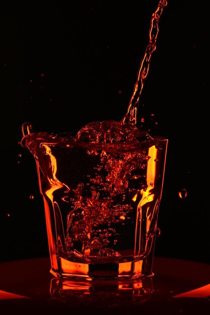 Gloomy still life with a glass. Orange water is poured into a whiskey glass