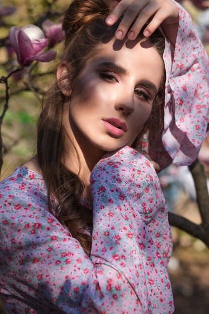 Glorious brunette woman posing near the flowering magnolia tree in fashionable dress