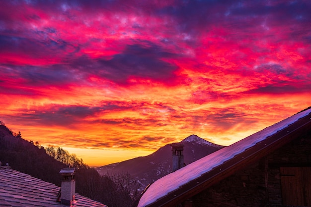 写真 イタリア アルプスの栄光の夕日 雪に覆われた谷の牧歌的な村と雪を頂いた山の頂上の美しい空 イタリア ピエモンテ州の冬