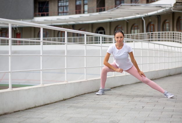 Glorious tanned athletic girl wearing sport apparel doing stretching workout at the stadium. Space for text