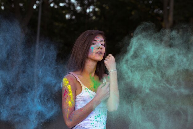 Glorious tanned woman with short hair posing with exploding Holi blue and green dry paint