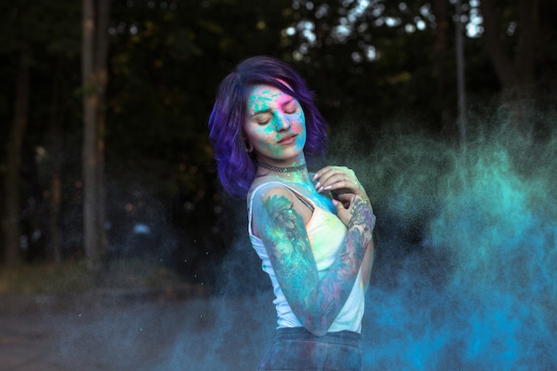 Glorious young woman with purple hair posing with exploding Holi powder at the park