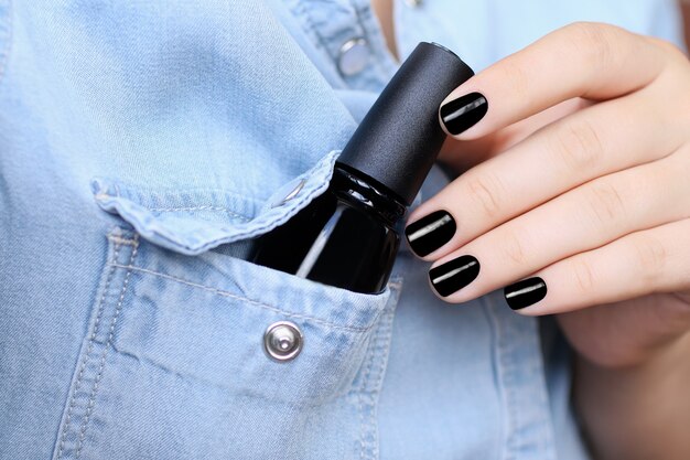 Glossy black manicureA female hand puts a bottle with nail polish in the pocket of a denim shirt