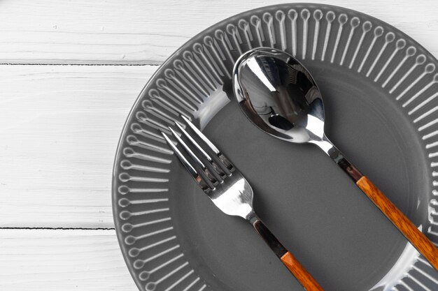 Glossy grey ceramic plate with cutlery on wooden kitchen table