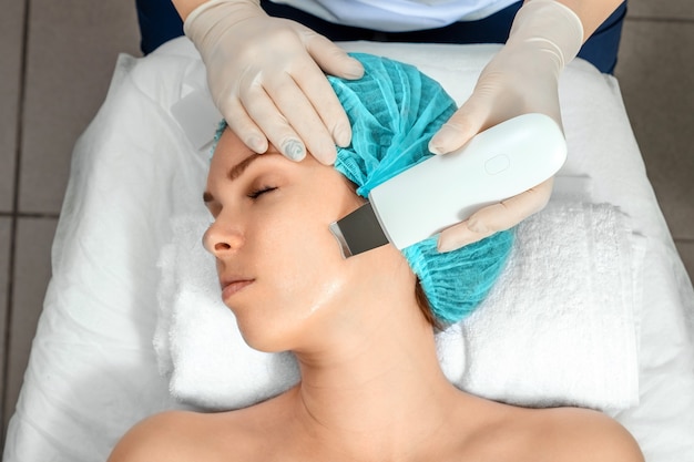A gloved beautician cleanses the skin on the face using a special gel and equipment