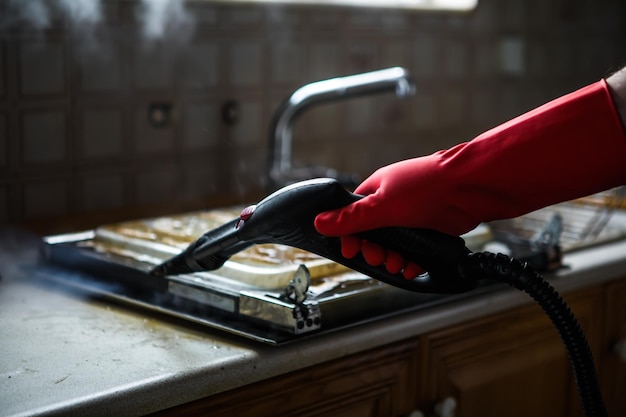 Gloved cleaner washing oven with steamer at home closeup