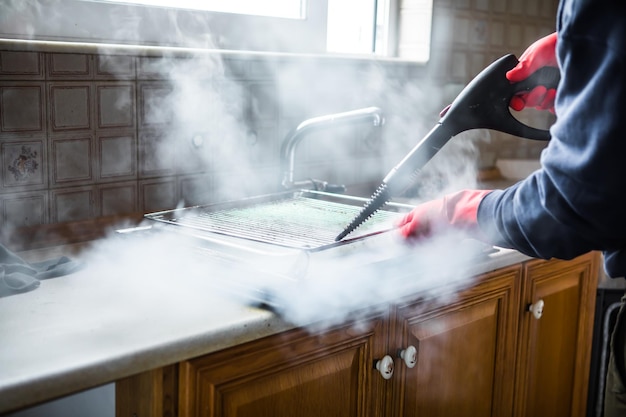 Gloved cleaner washing oven with steamer at home closeup