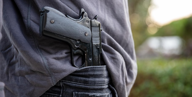 Gloved hand carrying a pistol in his pants blur nature background