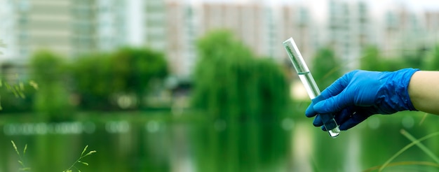 A gloved hand collects water into a test tube. sampling from\
open water in a city water body. scientist or biologist taking a\
sample of water in a test tube against the background of a\
cityscape.