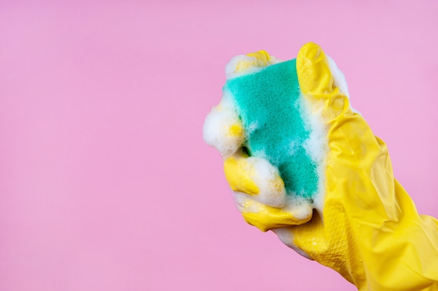 Foto la mano guantata tiene una spugna di schiuma su sfondo rosa