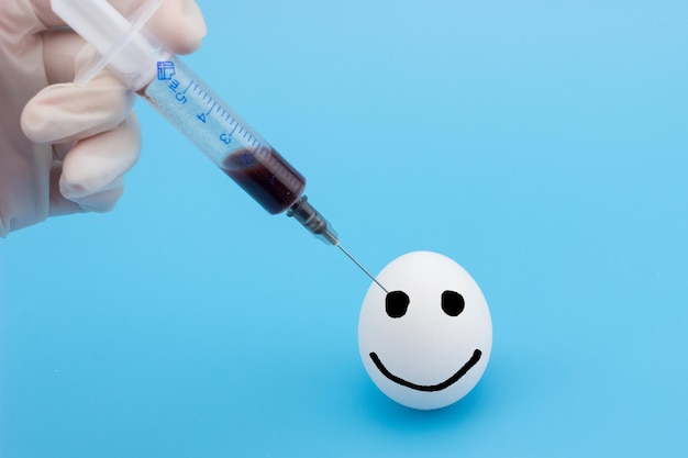 A gloved hand inserts a syringe into a chicken egg closeup on a blue background