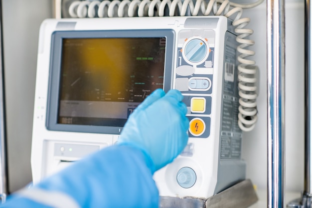 Gloved hand of paramedic going to press button on medical first aid equipment inside ambulance car