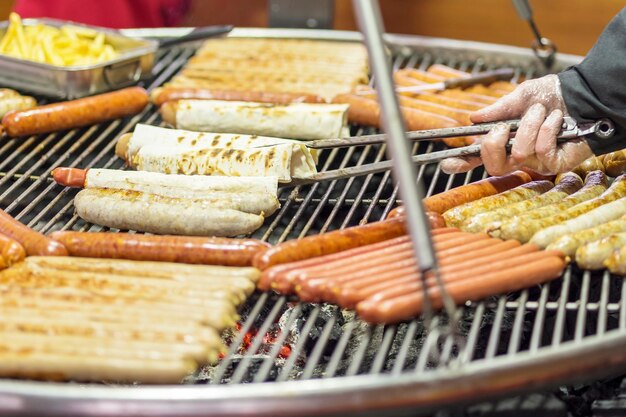 gloved hand turns barbecue sausage in pita bread on the grill