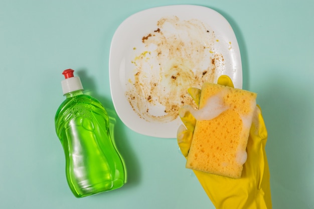 Photo a gloved hand with a foam sponge and detergent on the background of a dirty plate