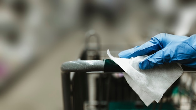 Gloved hand with a tissue paper on a shopping cart in a supermarket during the Coronavirus pandemic