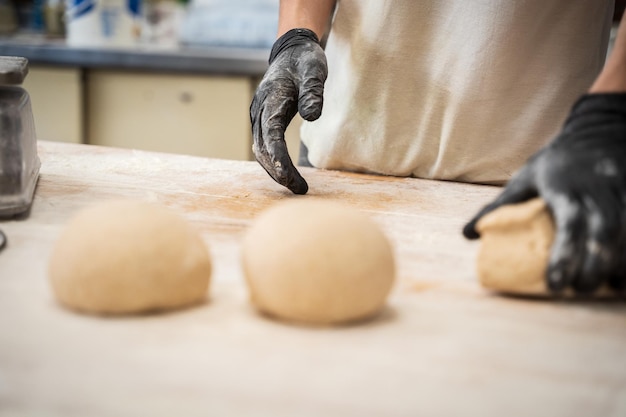 Gloved hands of a baker placing dough to make bread on a wooden table