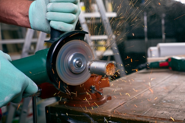 Photo gloved hands hold an angle grinder and cut the pipe, many sparks fly to the sides