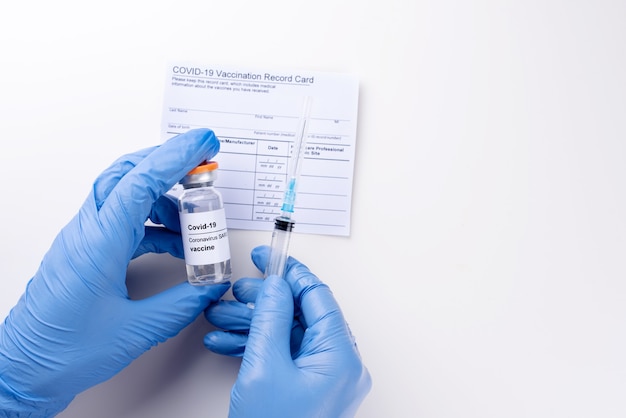 Gloved hands holding a vial with covid-19 vaccine and syringe, the vaccination record card, vaccination passport