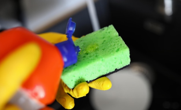 Gloved hands pour detergent for dishes on sponge