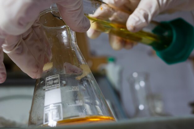 Photo gloved hands pour liquid from one flask into another against a blurred background