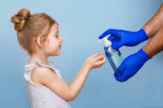 Le mani guantate versano sapone liquido nelle mani del bambino.