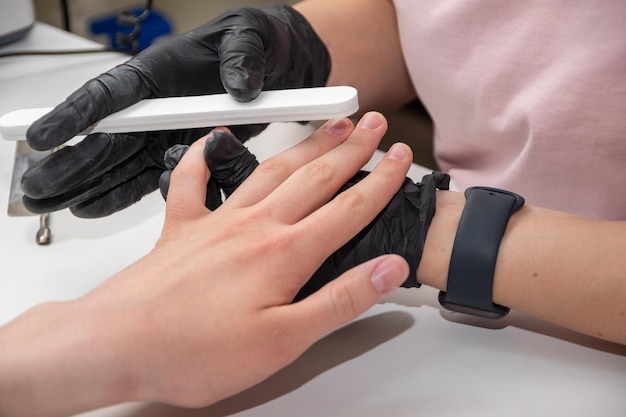 Gloved hands of a skilled manicurist filing a young woman's nails with a nail file Hands during a manicure care session in a spa salon Manicurist files nails with a nail file closeup