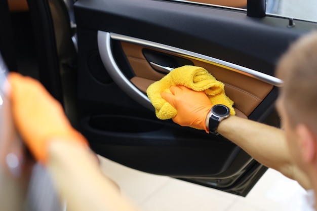 Gloved handyman wipes car doors inside cabin closeup