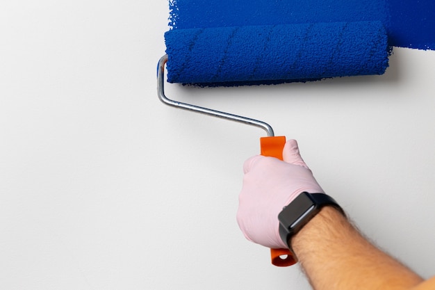 Gloved male hand painting wall into classic blue color