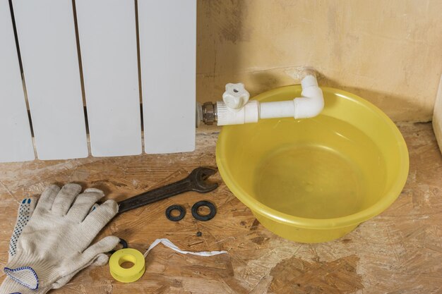 Gloves and repair tools near a leaking heating system. Accident of the heating system of a private house. Heating radiator.