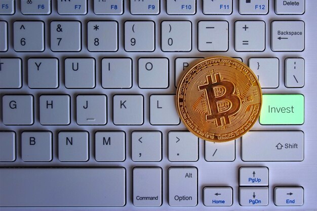 Glowing bitcoin on top of keyboard with text INVEST Cryptocurrency and technology concept
