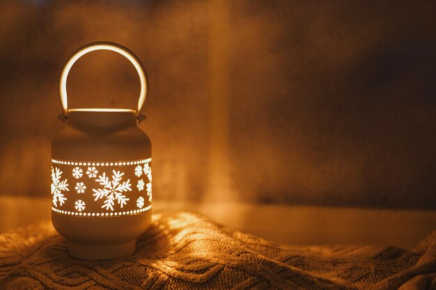 glowing christmas lantern with golden lights on cozy knitted sweater on frosty window sill in eve atmospheric magical still life merry christmas happy holidays winter wallpaper copy space