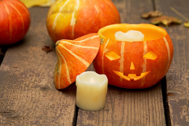 Incandescente zucca di halloween male, accanto a una candela bianca estinta su un vecchio pavimento in legno con foglie secche di autunno