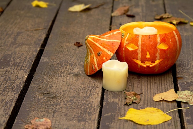 Светящаяся злая тыква Хэллоуина, рядом с белой потухшей свечой на деревянном старом полу с сухими осенними листьями
