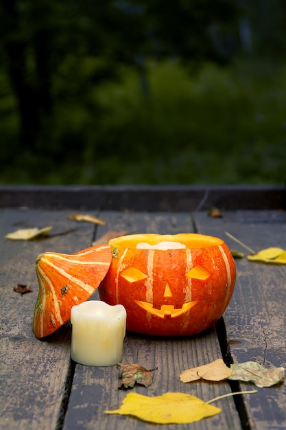 Foto incandescente zucca di halloween male, accanto a una candela bianca estinta su un vecchio pavimento in legno con foglie secche di autunno