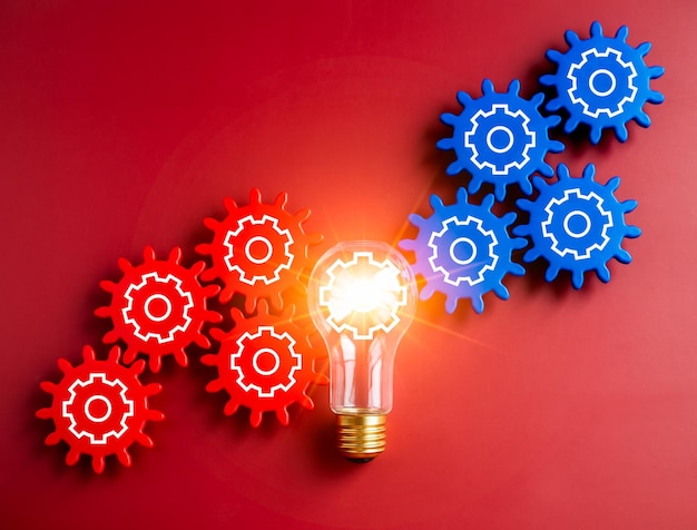 Glowing light bulb connected between blue and red gear wheels on red background Business strategy management and solution human research connection teamwork and creative idea concepts