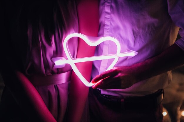 Glowing neon heart sign pierced by cupid arrow