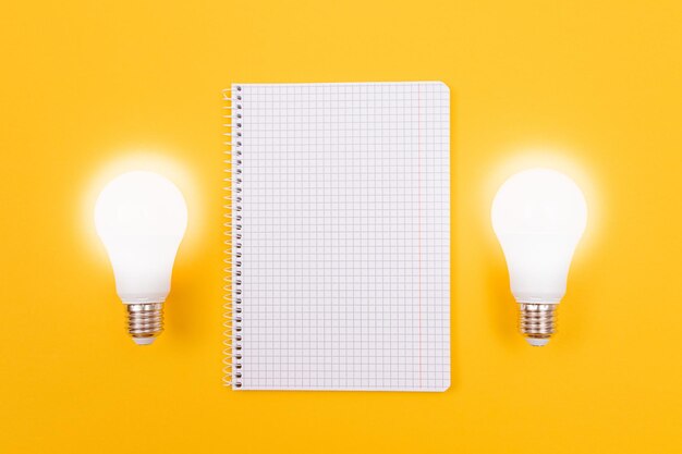 Glowing power saving lamp with notepad lying on yellow table