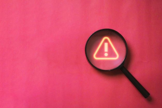 Photo glowing red triangle caution warning or exclamation sign inside magnifier glass for notification error and maintenance concept