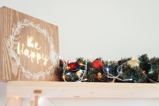 Foto immagine in legno incandescente quotbe happyquot decor element accanto alla ghirlanda dell'albero di natale sul ripiano del primo piano