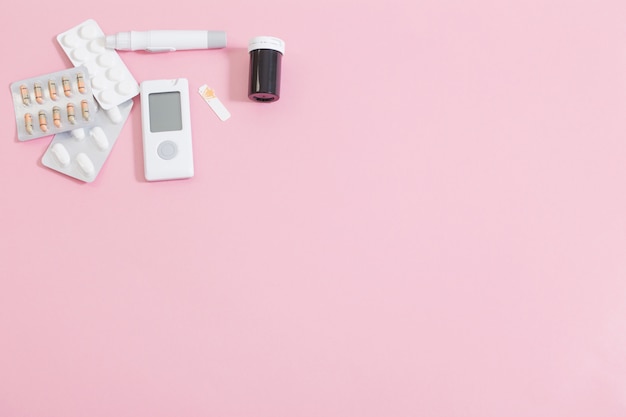 Glucometer and pills on pink table