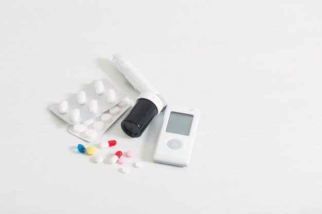 Glucometer and pills on white wooden table