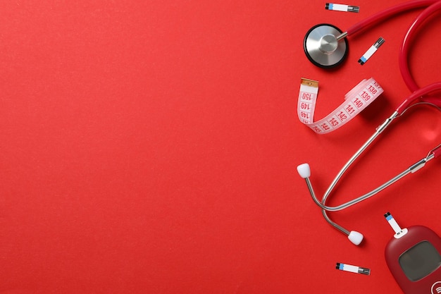 Glucometer stethoscope and measuring tape on red background space for text