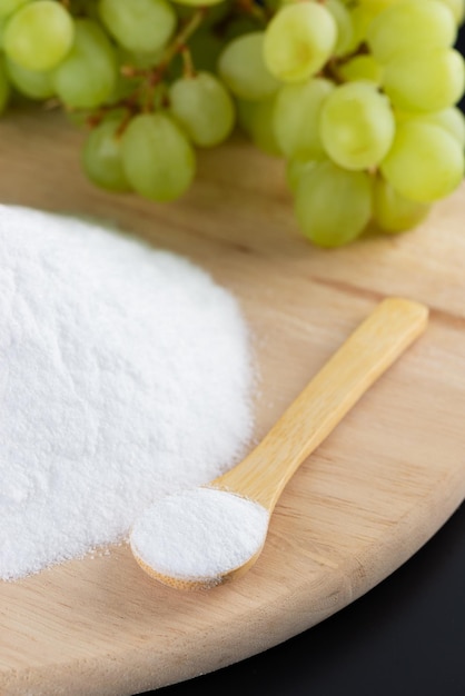 Photo glucose or grape sugar with a spoon fresh grape on a wooden board on a black background sweet food selective focus