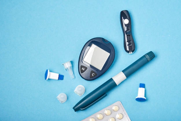 glucose meter, lancet, syringe and pills, needles for injection, blue background, copy place top view