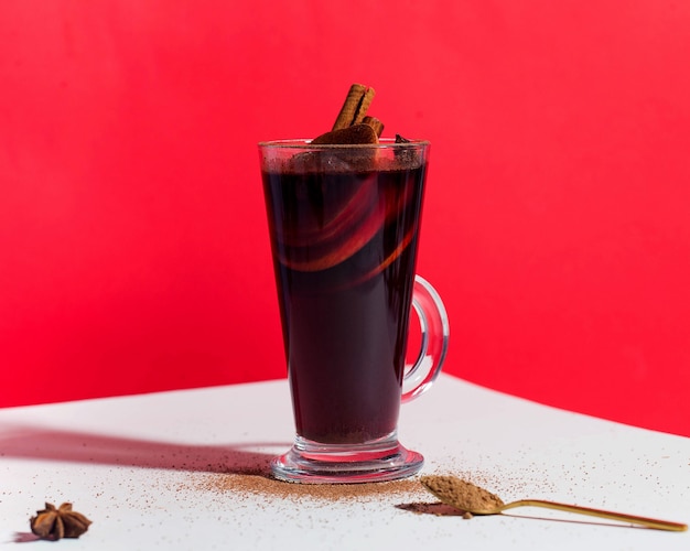 Glühwein in een glas met een kaneelstokje op rode achtergrondkruidenfoto met hard lichttrend