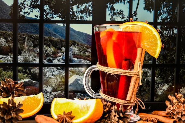 Glühwein Warme kerstdrank met kruiden op een vensterbank, naast het raam. Sinaasappelschijfjes, kaneelstokjes, dennenappels. Vakantiesfeer, rustieke stijl. Het idee om wenskaarten te maken