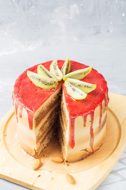 Photo gluten-free cake with strawberry frosting, coconut chips and almonds on a stand, decorated with kiwi slices. front slice of the cake. copy space. vertical position